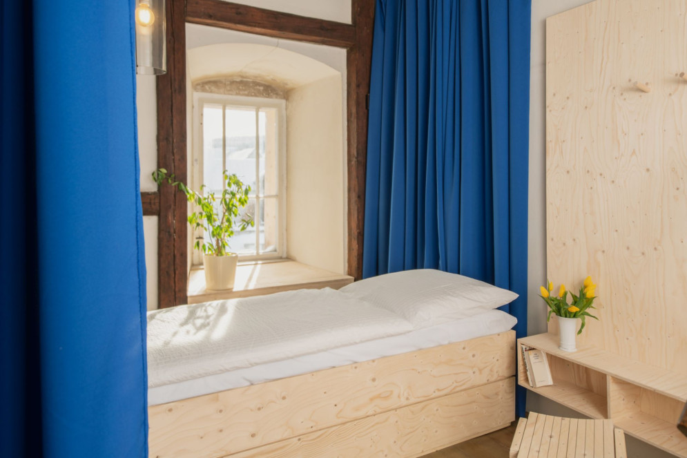 Ein weiß bezogenes Holzbett, umgeben von blauen Vorhängen an einem Fenster