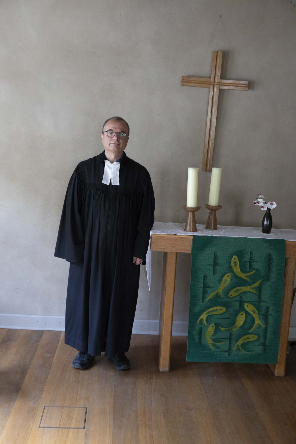 Pfarrer Lenz vor einem Altar mit zwei Kerzen und Holzkreuz an der Wand.